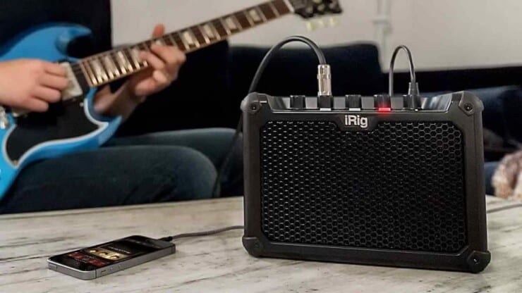 guitarist playing guitar with smartphone connected to amp on table