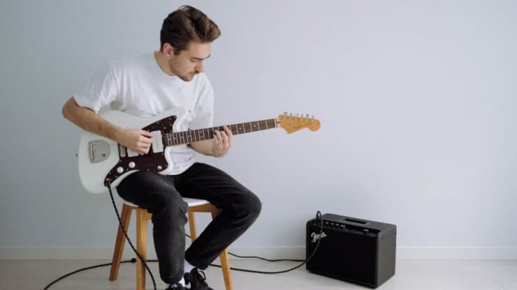 how to make a guitar amp sound better - guitarist sitting while playing guitar that is connected to amp