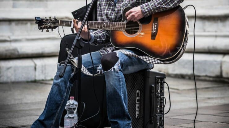 person sitting on a guitar amp, playing guitar, performing outside