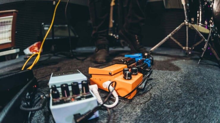 person playing guitar with guitar pedals and amps on the floor