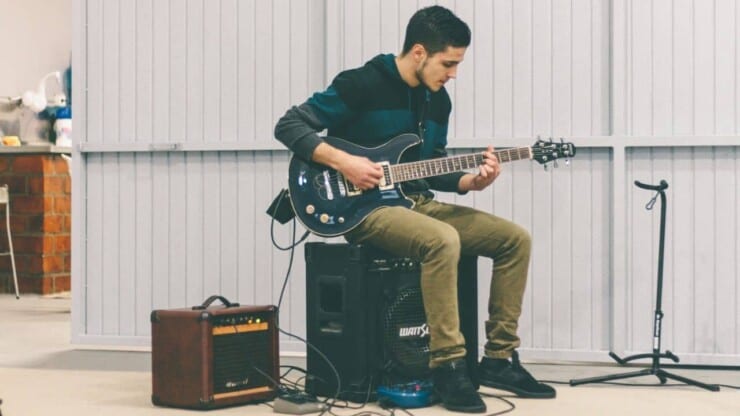 how to use a guitar amp - man playing guitar with amps