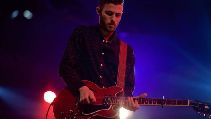 man guitarist playing electric guitar with capo on stage